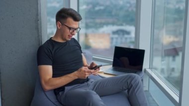 Adam çalıştığı bilgisayarı kaldırdı. Gözlüklü bir iş adamı akıllı telefonunda bir şeyler yazıyor. Kapatın. Bulanık arkaplan.