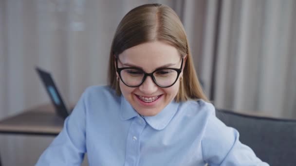 快乐地微笑着 长发女士戴着眼镜 牙齿上戴着牙套 看着电脑屏幕 办公室里快乐的员工 — 图库视频影像
