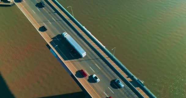 片道の複数車線の高速道路で橋で移動する車の後 グリーンウォーターの背景にある橋の上の晴れた映像 トップビュー — ストック動画