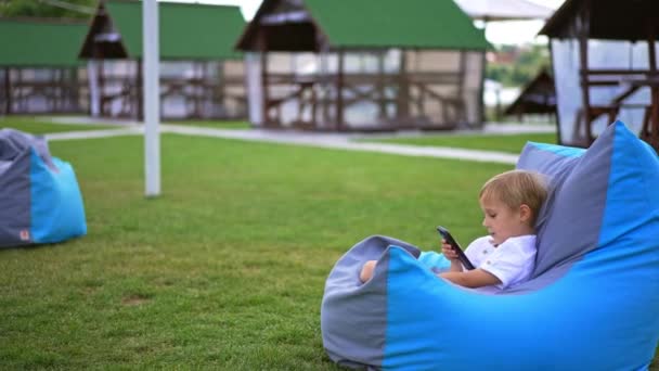 Malý Šestiletý Blonďatý Chlapec Sedí Pohodlně Křesle Telefonem Ruce Dítě — Stock video
