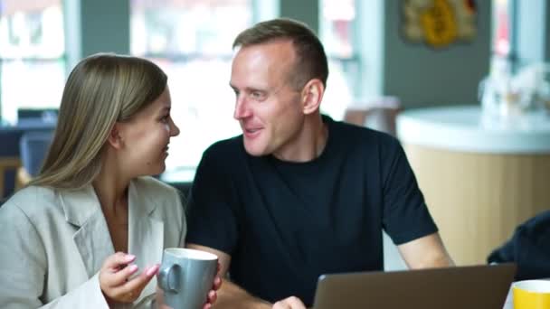 男人和女人坐在咖啡馆里 面前放着笔记本电脑 情侣们在聊天 喝咖啡 靠近点模糊的背景 — 图库视频影像