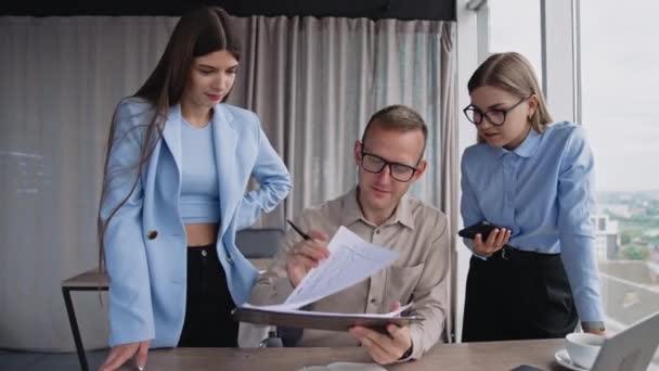 中年男人坐在办公桌前看文件 两个女同事站在他的两边 寻找问题的解决方案 — 图库视频影像