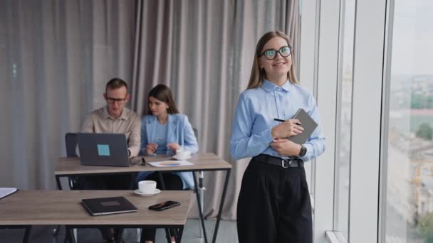 成功的 自信的女商人在笔记本里翻阅笔记 靠近点两名同事在后台的办公桌前工作 — 图库视频影像