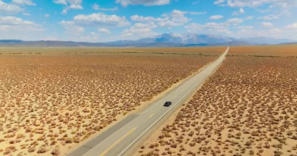 跟着黑色的汽车沿着空旷的道路穿过荒无人烟的土地 从加州到内华达州的高速公路在阳光灿烂的日子里拍摄到的画面 背景中的山 — 图库视频影像