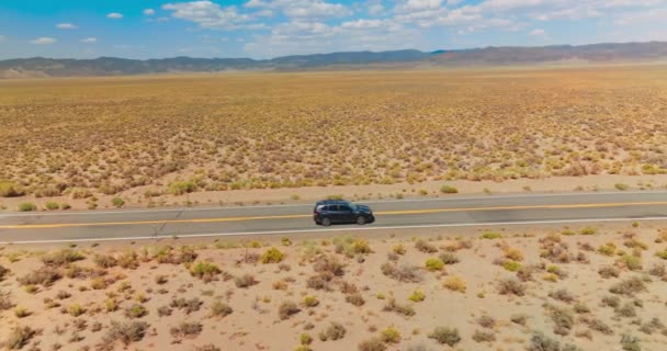 在阳光灿烂的沙漠中 汽车在空旷的路上行驶 蓝云天背景下的高山地平线 — 图库视频影像