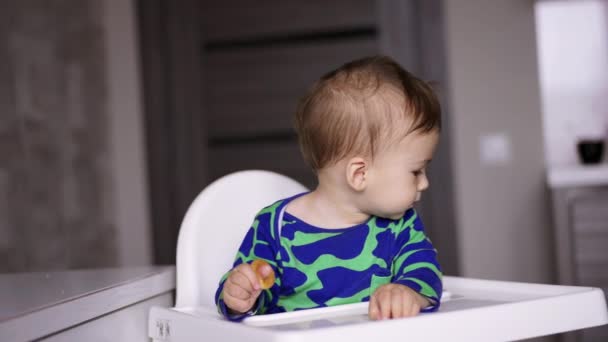 可爱的小孩穿着蓝绿相间的衬衫坐在餐桌旁 妈妈正在给她的孩子一个大勺子 他拿去了 模糊的背景 — 图库视频影像