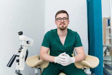 Diş muayenehanesinde sandalyede oturan yeşil üniformalı erkek dişçinin portresi..