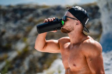 Sahilde idmandan sonra kaslı bir adam su içiyor..
