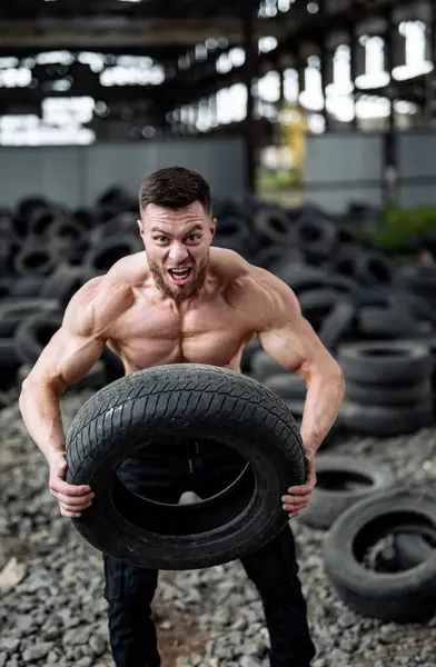 Muscular man lifts tire in the gym.