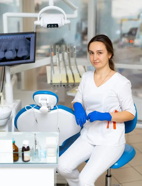 Young female dentist sits in chair in dental office.