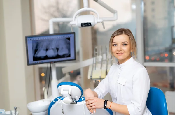 Female dentist sits in chair in front of dental x-ray machine.