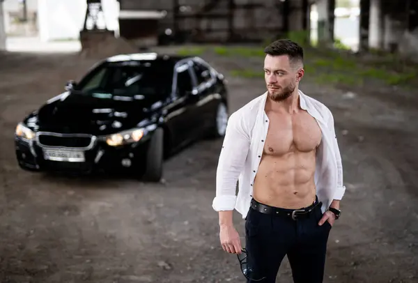 Handsome man stands next to black car and car with beautiful body.