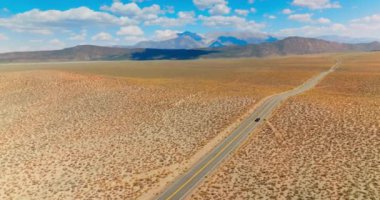 Nevada, ABD yolunda yapayalnız siyah bir araba. Mavi gökyüzüyle çelişen güzel bir çöl manzarası. Arkaplanda dağlar.