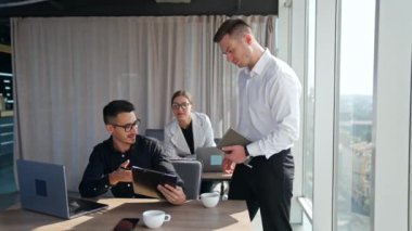 Ofis ekibi belgeleri tartışıyor. Ön masadaki adamlar dosyaları ve bayan çalışanları tutarak kağıtlara işaret eden önerilerde bulunuyorlar..