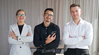 Kendinden emin genç ofis ekibi kameranın önünde gülümsüyor. İş arkadaşları yeni zorluklara ve görevlere hazır.