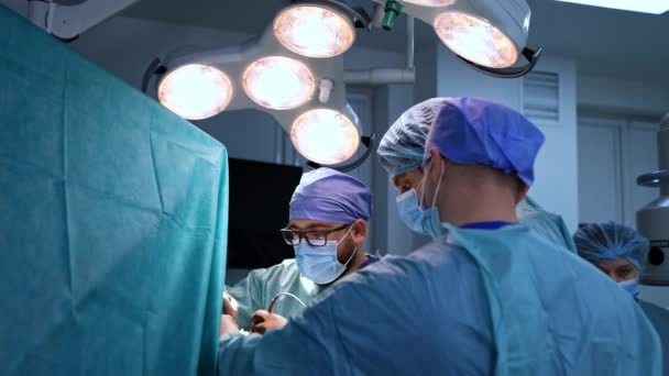手術室で明るいランプの下で働く外科医のチーム 外科手術で協力する男性医師 — ストック動画
