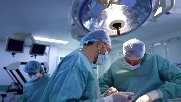协同工作的外科医生在操作时使用现代的工具装置 女护士站在后面 模糊的背景 — 图库视频影像
