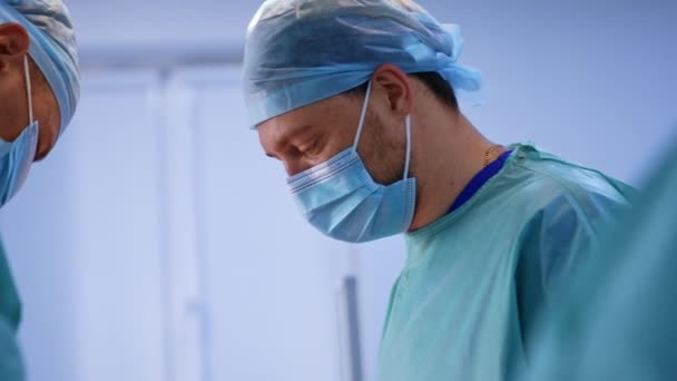在现代手术室工作的戴帽子戴面具的医生 一位男性外科医生的侧像集中在他的工作上 模糊的背景 — 图库视频影像