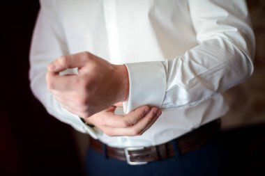 Adam kol düğmesi gömlek ve pantolon giyiyor..