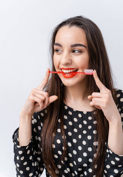 Young woman brushing her teeth with red toothbrush isolated on white.