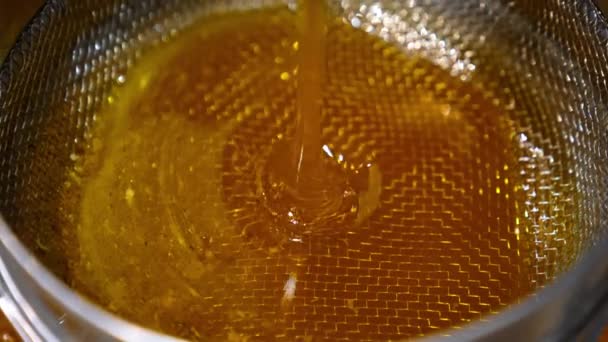 金色的新鲜蜂蜜从机器上漏出 蜂蜜倒在金属筛子上过滤蜡碎片 靠近点 — 图库视频影像