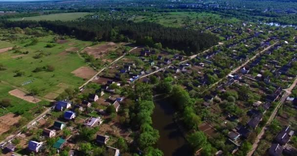 河岸上美丽的绿色村庄的全景 在阳光灿烂的日子飞越闪亮的水面 背景下的大城市 — 图库视频影像