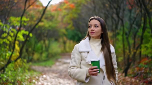 美丽的长发女人手里拿着纸杯在公园里散步 夫人享受大自然温暖的秋日 模糊的背景 — 图库视频影像