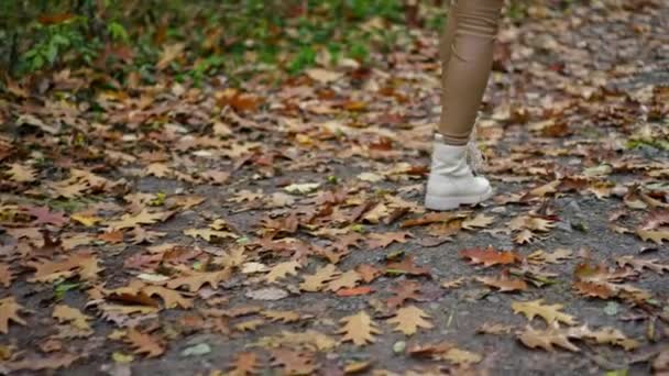 身着米黄色紧身裤和白靴的女性在公园的小径上走得很快 不为人知的女士在秋日散步 — 图库视频影像