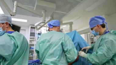 Cerrahlar operasyon odasında kamera karşısında sırtüstü duruyorlar. Başhekim ameliyatın sonunda hastanın omzunu dikiyor..