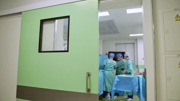 操作テーブルで働く制服の外科医のグループ 現代の手術室への扉を開けて立っている — ストック動画
