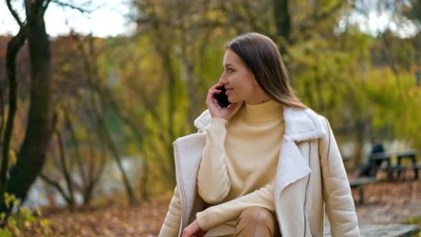 Sonbahar Parkında Oturmuş Telefonda Konuşan Rahat Gülümseyen Bayan Esmer Genç — Stok video