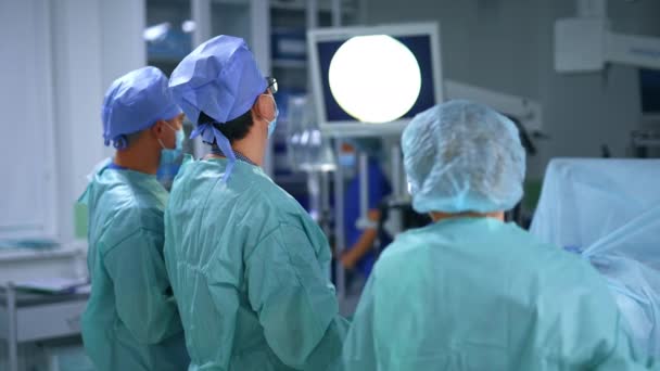 外科手術で作業する外科チーム 医師はカメラに背中を向け 目の前にあるモニターを注意深く見ている — ストック動画