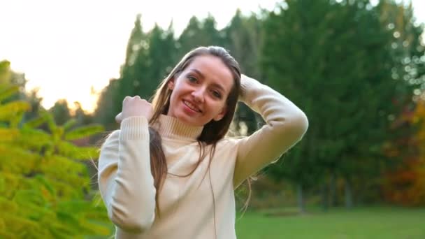 暖かい白いセーターに触れ 彼女の長い髪を振って笑顔のコーカサス人女性 秋の公園で屋外で過ごした楽しい時間 — ストック動画