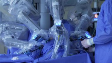 Cerrah modern cerrahide robot ekipmanlarıyla işbirliği yapıyor. Doktorun elinde bir alet tutarken plastik içinde robot kollar yavaşça hareket ediyor..