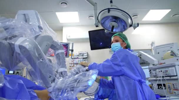 青いユニフォーム マスク キャップを着用した医薬品は プラスチックで覆われた装置のロボット腕を動かします 最小限の侵略の近代的な手術で使用される先進技術 — ストック動画