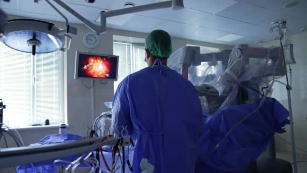 ロボット機器の助けを借りて手術を行った ドクターは彼の目の前の壁のスクリーンを見ているカメラの背中に立っています — ストック動画