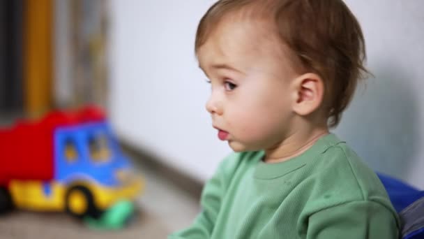 素敵な赤ちゃんが驚きのカメラを見ている クローズアップ 子供は床に座り 周りのおもちゃを持っています ブラーレッド バックドロップ — ストック動画