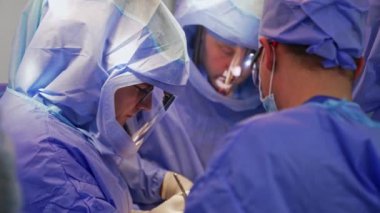 Koruyucu giysiler giyen cerrahlar metal aletlerle çalışıyorlar. Profesyonel doktorlardan oluşan bir ekip ameliyatta işbirliği yapıyor..