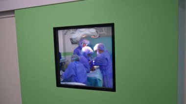 Cerrahi tiyatronun kapısında küçük kare bir pencere var. Operasyonel tiyatroda çalışan cerrahlardan oluşan tıbbi bir ekip..