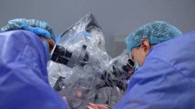 Üniformalı, maskeli ve şapkalı erkek ve kadın sağlıkçılar mikroskoba dikkatle bakıyor. Yüksek teknoloji ekipmanları plastikle kaplıdır. Düşük açı görünümü.