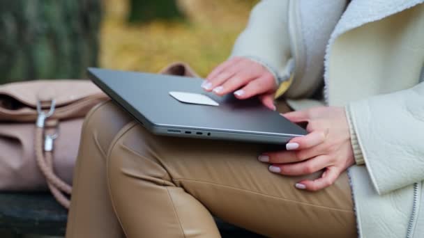 女性の手はベージュパンツの膝の上に横たわるノートパソコンを開けます 屋外に座っている女性は オフィスから出るつもりです — ストック動画