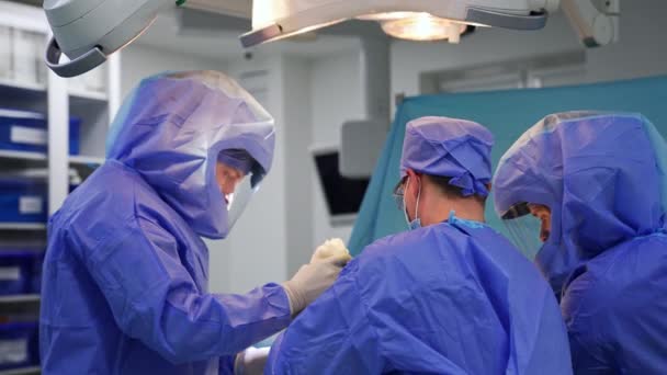 三个外科医生在手术室工作 两名医生穿着防护服 一名医生穿着普通外科医生的衣服 — 图库视频影像