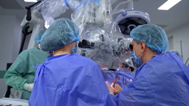Мужчина Нейрохирург Ассистент Медсестра Рассматривают Микроскоп Операционной Задний Вид Занятых — стоковое видео
