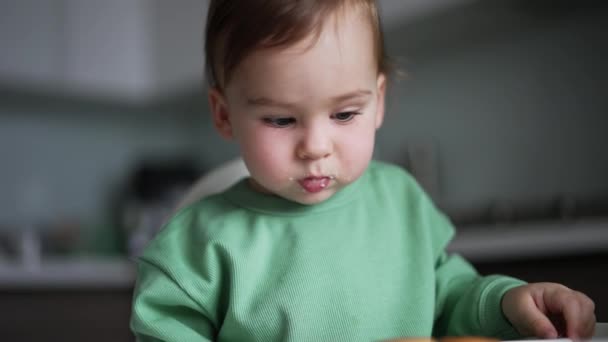 嘴边衔着食物的可爱的小宝宝坐在餐桌旁 妈妈的手指向他面前的百吉饼 孩子们注意地看着 — 图库视频影像