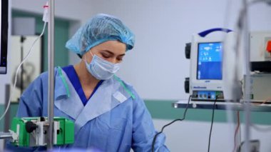 Ameliyat odasındaki ekipmanın yanında duran beyaz kadın hemşire. Sıhhiye teli aparattan ayarlar ve gider..