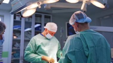 Birkaç cerrah tarafından yapılan estetik ameliyat. Hemşire ve anestezi uzmanı hastanın ayaklarının dibinde duruyor. Modern işletim odası arkaplanı.