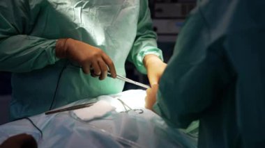 Bej lateks eldivenli üniformalı cerrah iş başında elektrikli cihaz kullanıyor. Metal aletler ve bant doktorun yaklaşımında hastanın üzerinde..