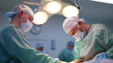 Tıbbi uzman ve asistanı ameliyathanede çalışıyor. Estetik ameliyat yapan iş birlikçi doktorlar. Arka planda güçlü lambalar bulanık.