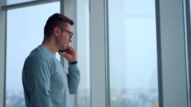 Beyaz bir erkek birini arıyor ya da telefona cevap veren birini dinliyor. Ofis penceresinde akıllı telefon kullanan bir işadamı..
