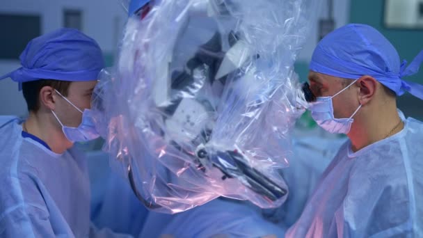Два Хирурга Мужчины Внимательно Смотрят Бинокль Микроскопа Современной Операционной Передовое — стоковое видео